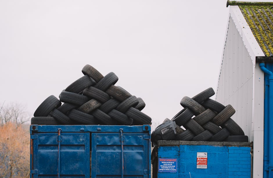 A large blue metal container filled with a substantial pile of used black rubber tires, stacked haphazardly with some tires leaning and overlapping each other. The tires vary slightly in size but are